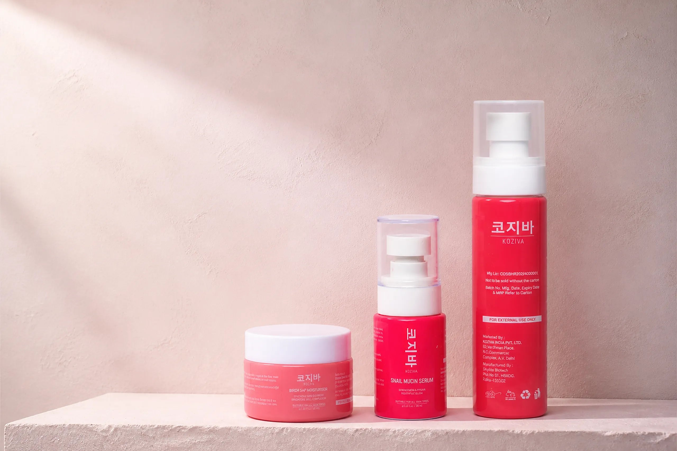 The three Koziva products together on a pink plaster ledge: the rice toner, the snail mucin serum and the birch sap moisturiser