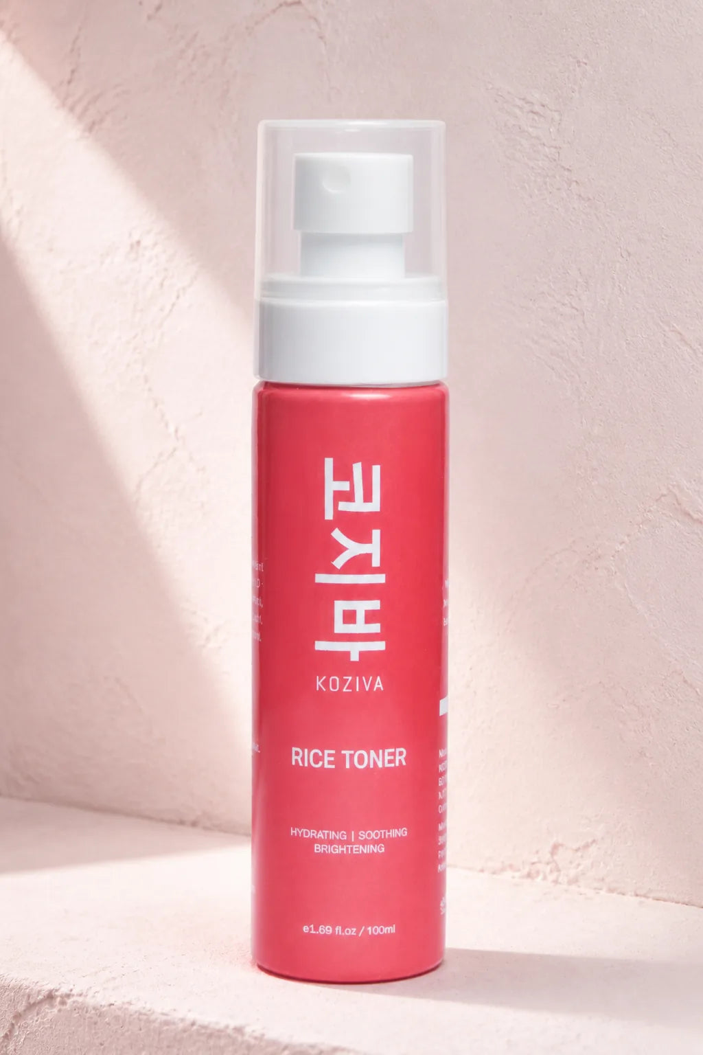 The Koziva rice toner bottle on a pink plaster ledge