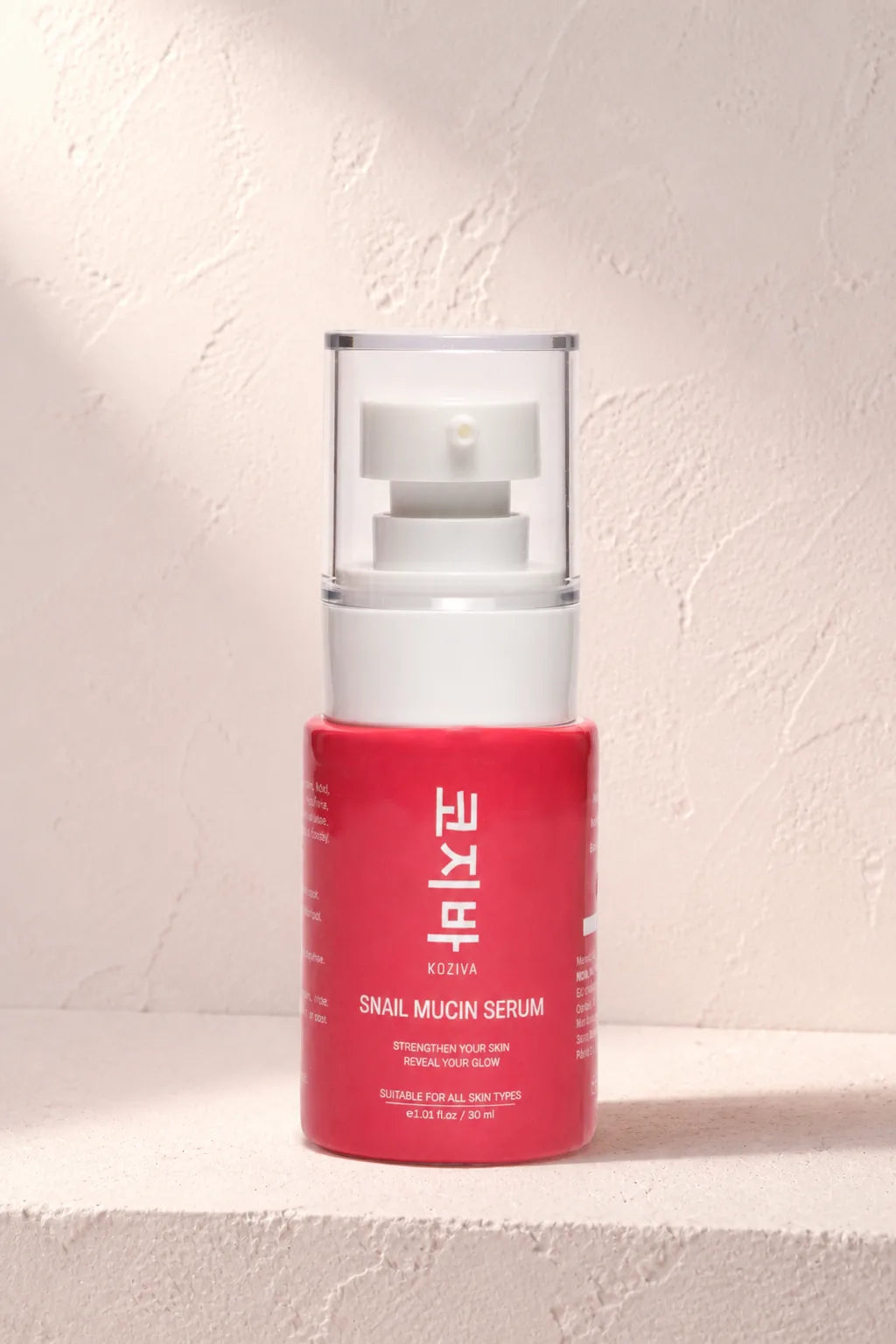 The Koziva snail mucin serum bottle on a pink plaster ledge