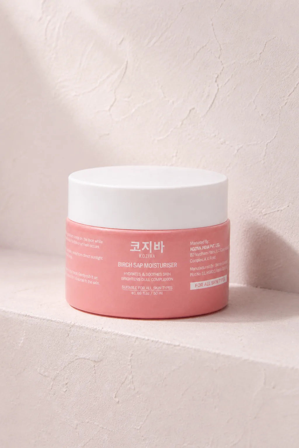The Koziva birch sap moisturiser jar on a pink plaster ledge