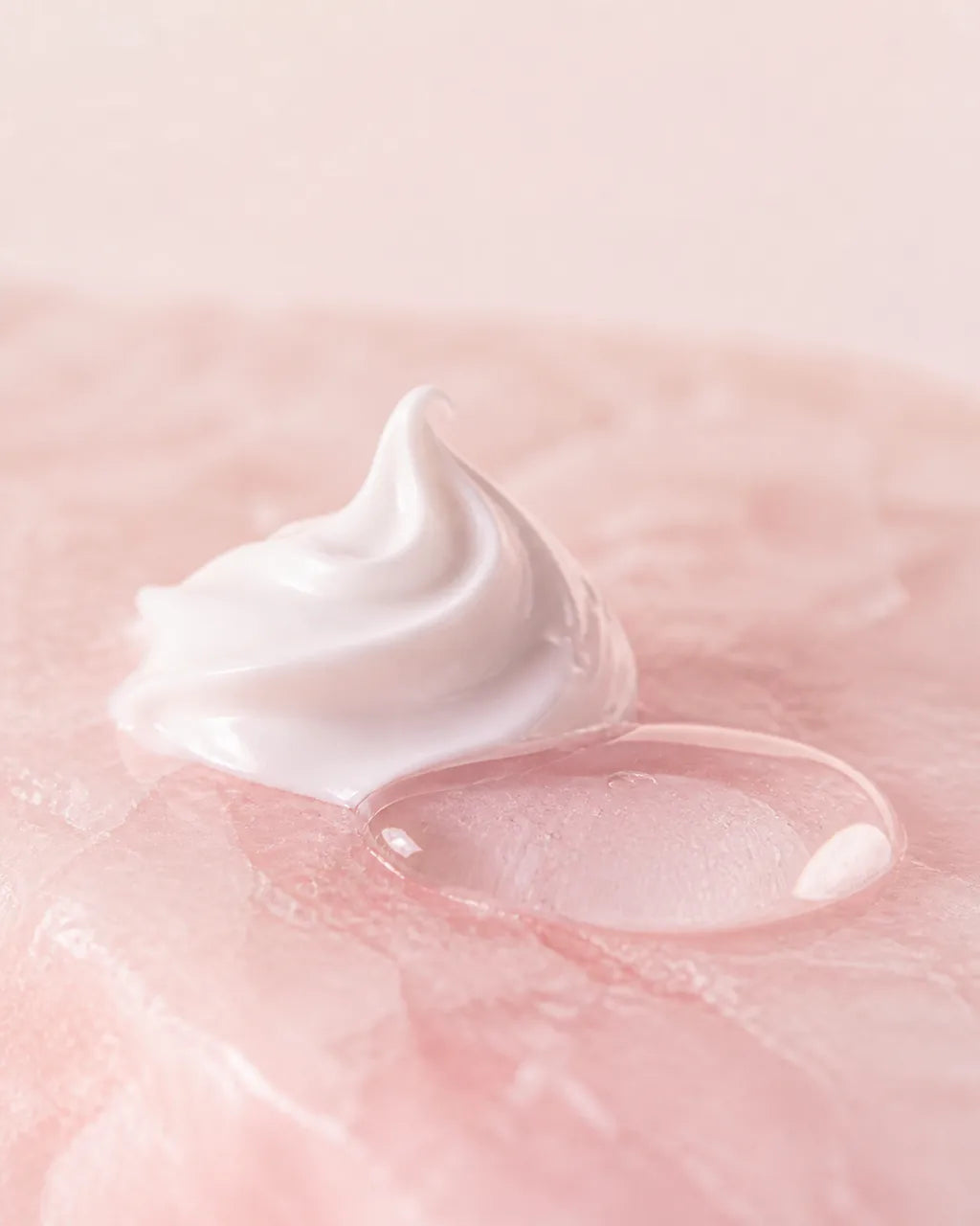 Close up of a swirl of white moisturiser on pale rose stone beside a bead of clear watery sap