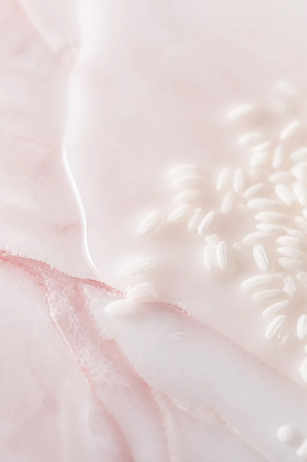 Close up of milky rice ferment liquid pooled on pale rose stone, with grains of white rice half submerged at the edge