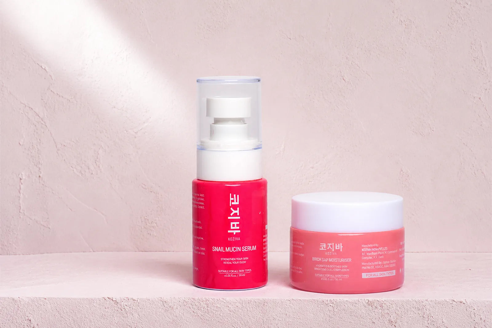 The Koziva snail mucin serum standing beside the birch sap moisturiser jar on a pink plaster ledge